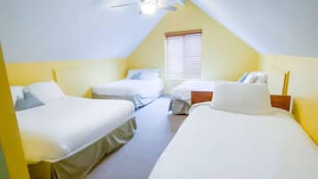 Un dormitorio tipo buhardilla triangular con tres camas individuales, un ventilador de techo y una ventana con persianas.