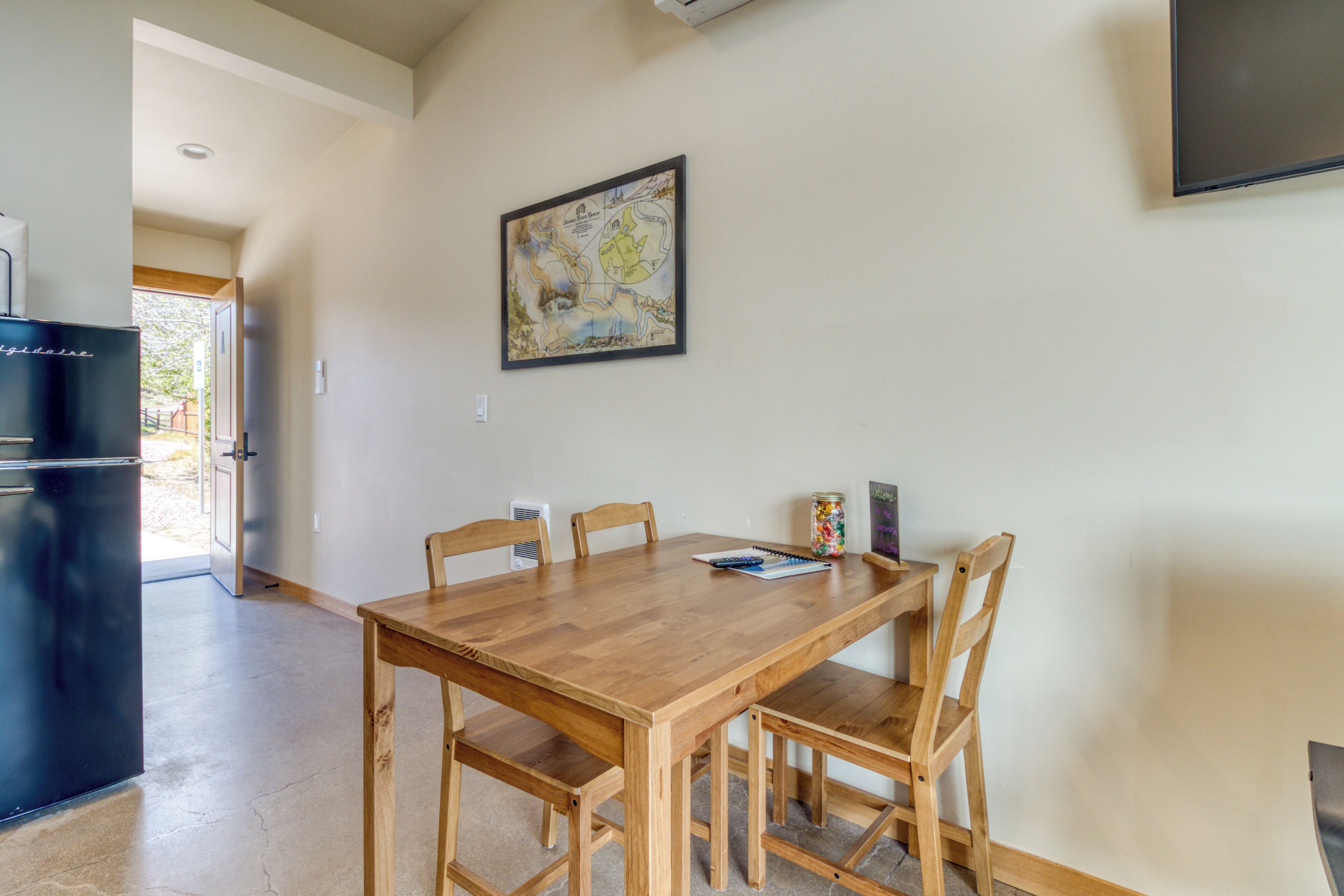 Un coin repas avec une table et des chaises en bois, un réfrigérateur noir et un téléviseur fixé au mur.