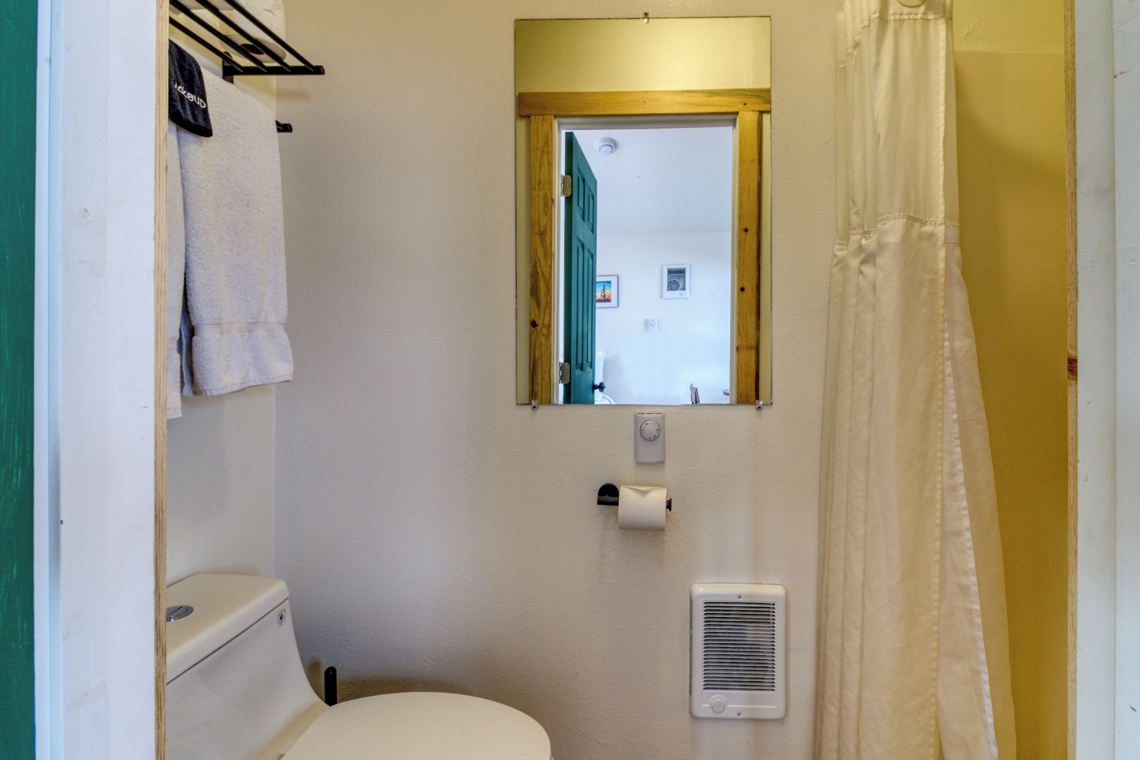 A small bathroom with a toilet, a towel rack, a mirror, a shower curtain, and a vent.