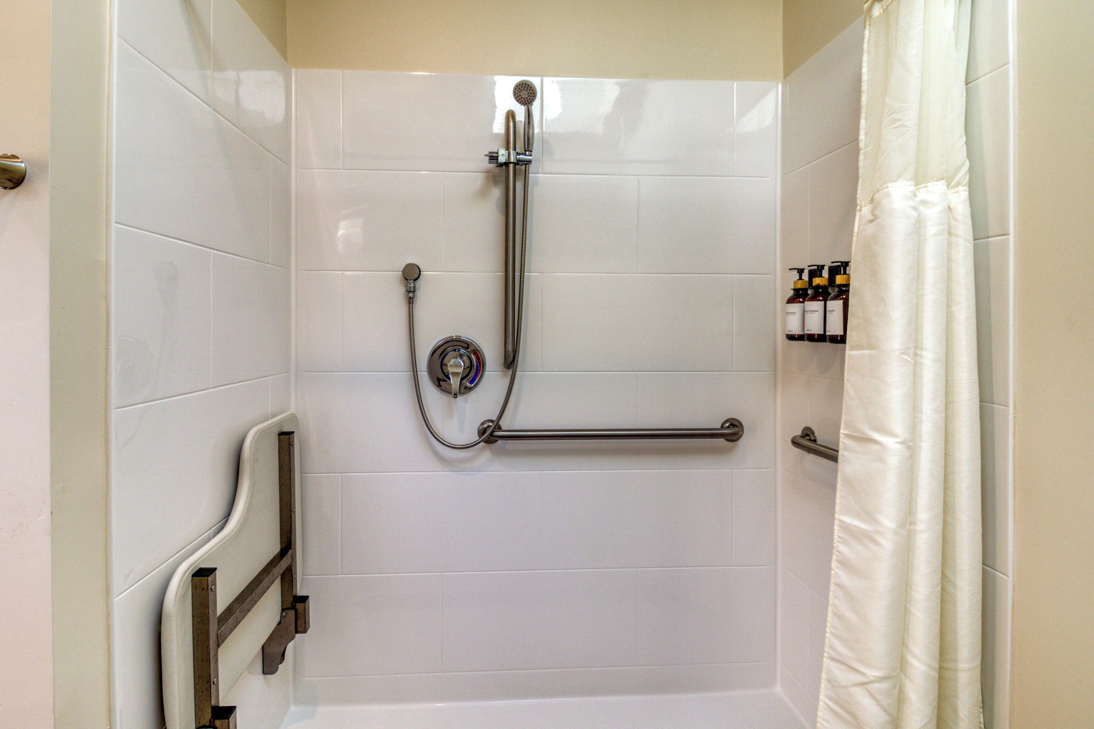 A shower area with a grab bar, a handheld showerhead, and a shower curtain.