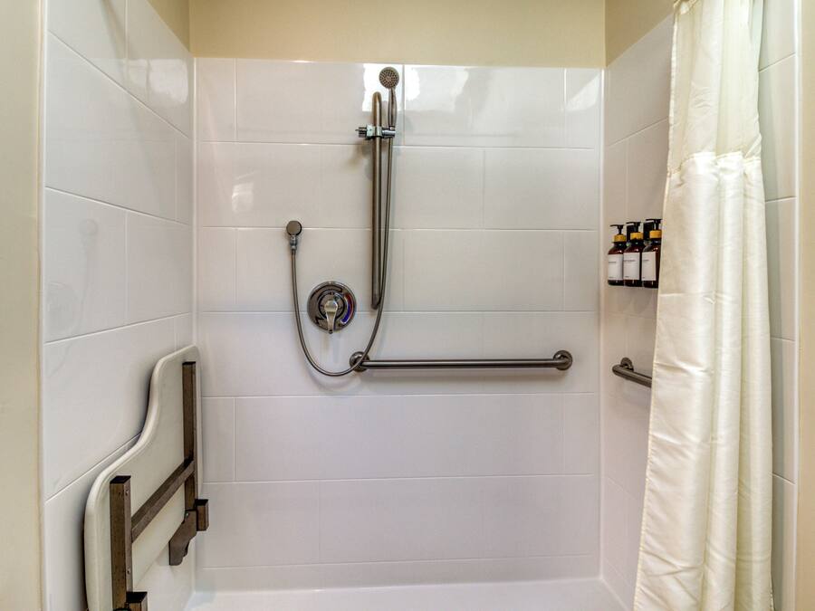 A shower area with a grab bar, a handheld showerhead, and a shower curtain.