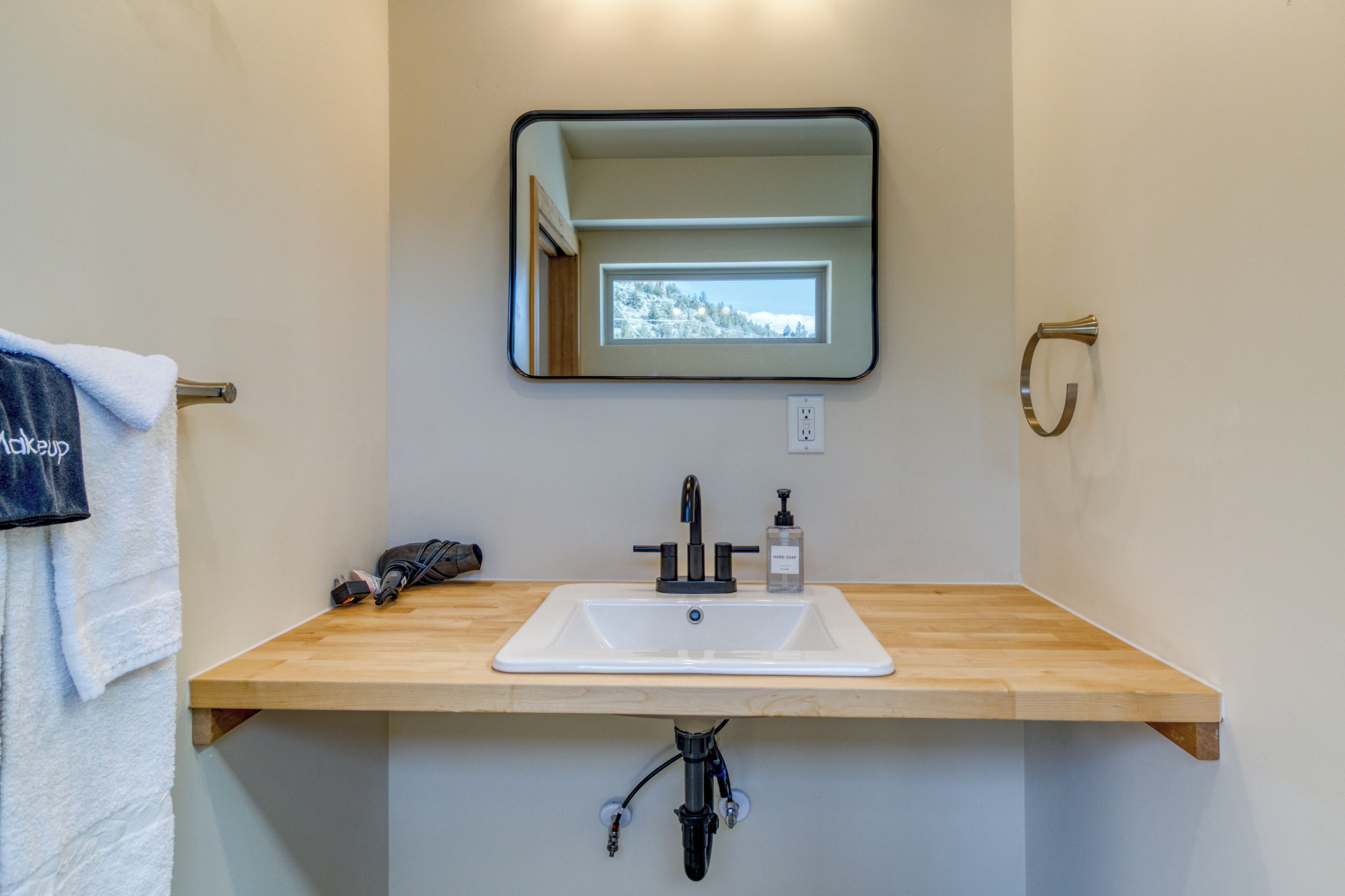 Une salle de bain avec un meuble-lavabo en bois, un lavabo blanc, un miroir et un porte-serviettes.