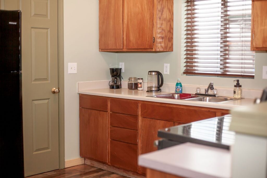A kitchen with wooden cabinets, a coffee maker, a kettle, and a sink.