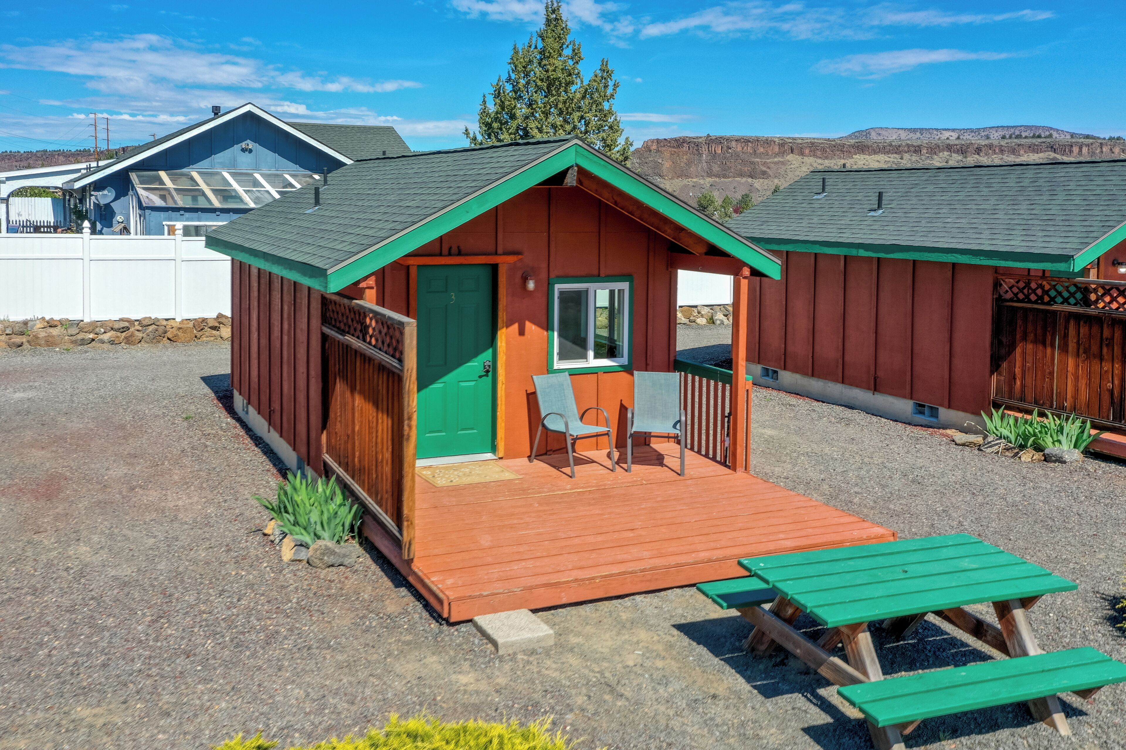 A small wooden cabin with a porch, two chairs, and a table.
