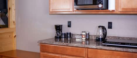 A kitchen with wooden cabinets, a microwave, a coffee maker, and a kettle on the countertop.