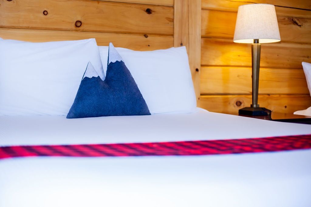 A bed with white linens, a blue pillow, and a red and black patterned throw.