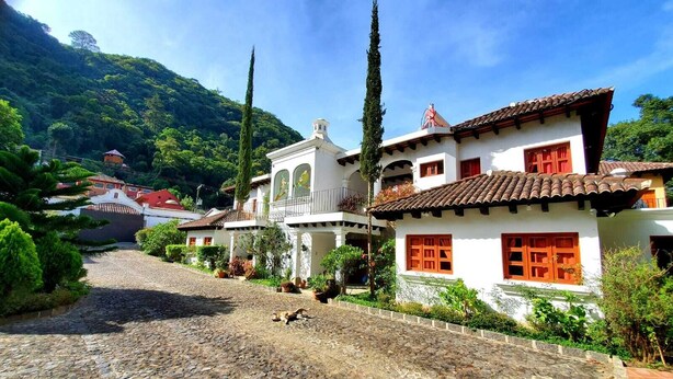 A cobblestone street leading to a white building with red shutters and a balcony.