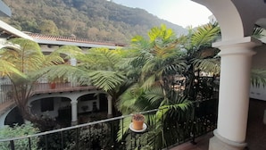 A balcony with a view of a lush garden and a mountain in the background.