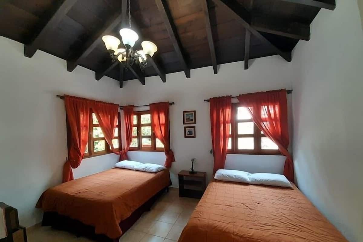 A room with two beds, each with an orange bedspread and white pillows, a wooden ceiling, and a chandelier.