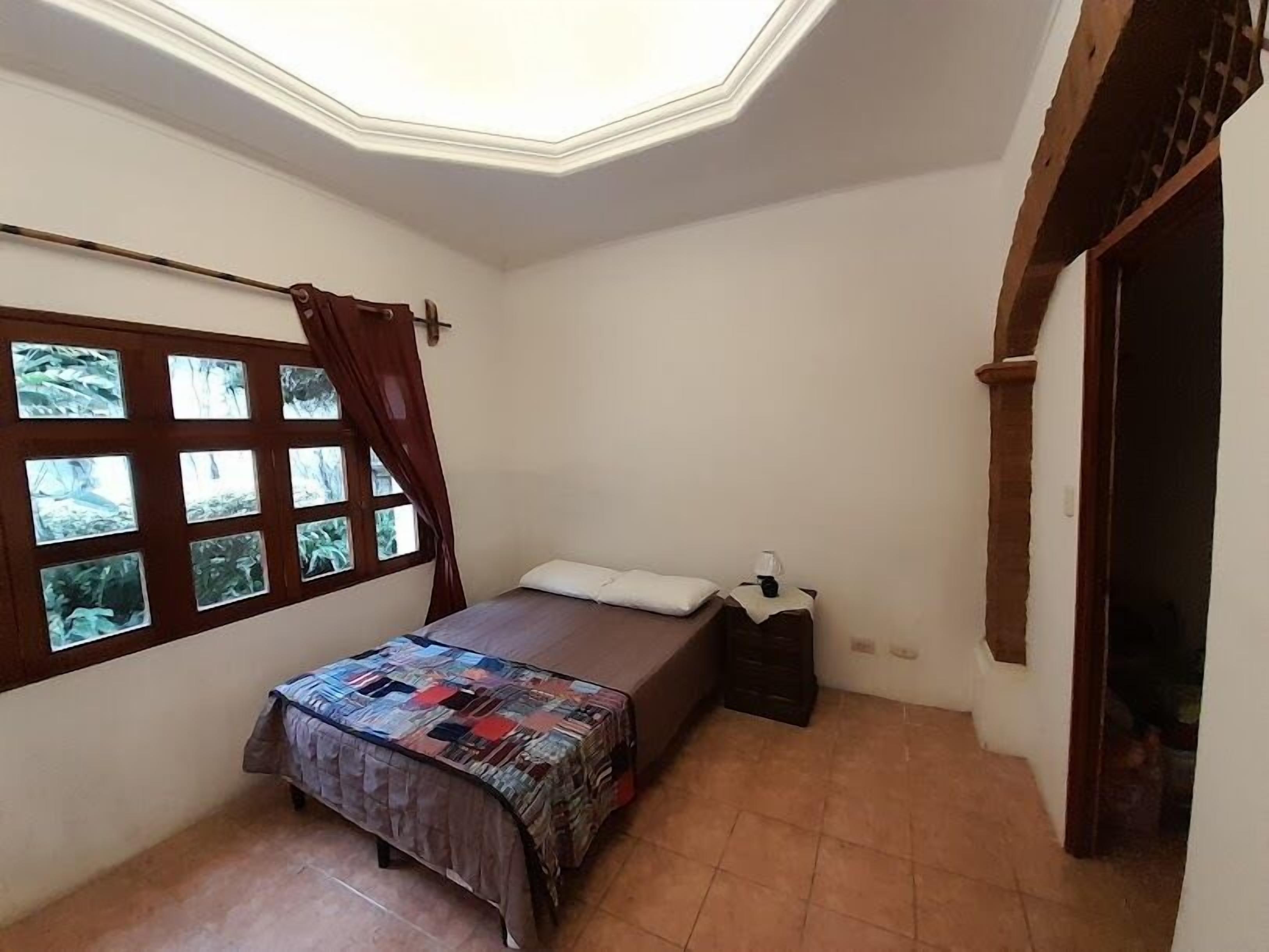 A bedroom with a bed, a window with curtains, a small bedside table, and a skylight.