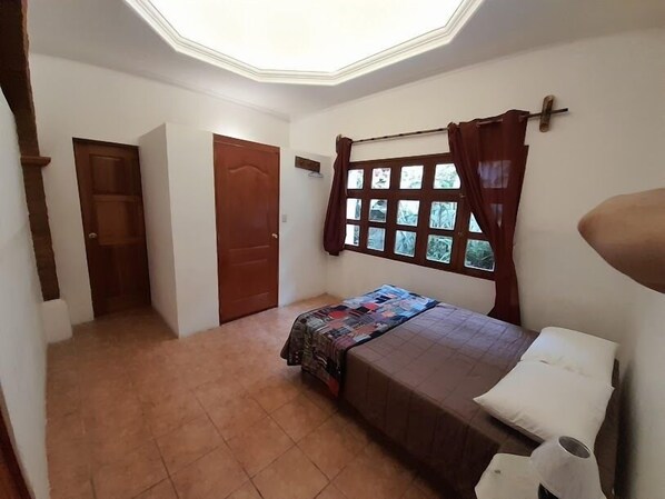 Un dormitorio con cama, una ventana con cortinas, una puerta y un tragaluz.
