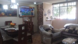 A living room with a sofa, a chair, a dining table with chairs, a TV mounted on the wall, and a window with bars. - Apartment Quinto #2 (Quito)