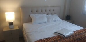 A hotel room with a bed, a nightstand with a lamp, and a suitcase. - Apartment Quinto #2 (Quito)