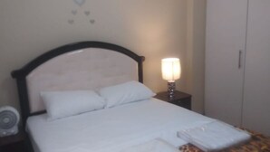 A neatly made bed with white linens, a bedside table with a lamp, and a wardrobe in a hotel room. - Apartment Quinto #2 (Quito)