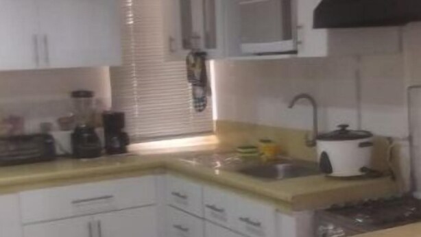 A kitchen with white cabinets, a yellow countertop, and a black range hood. - Apartment Quinto #2 (Quito)