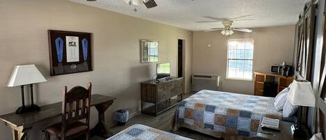 A hotel room with two beds, a desk, a chair, a TV, and a ceiling fan.
