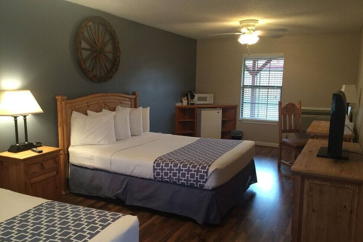 A hotel room with a bed, bedside tables, a desk, a chair, a microwave, a television, and a window with blinds.