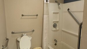 Ein Badezimmer mit Toilette, Haltegriffen, Dusche und Badewanne.