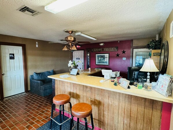A reception area with a wooden counter, two brown stools, a ceiling fan, and a sign that reads "HAPPY TRAILS".
