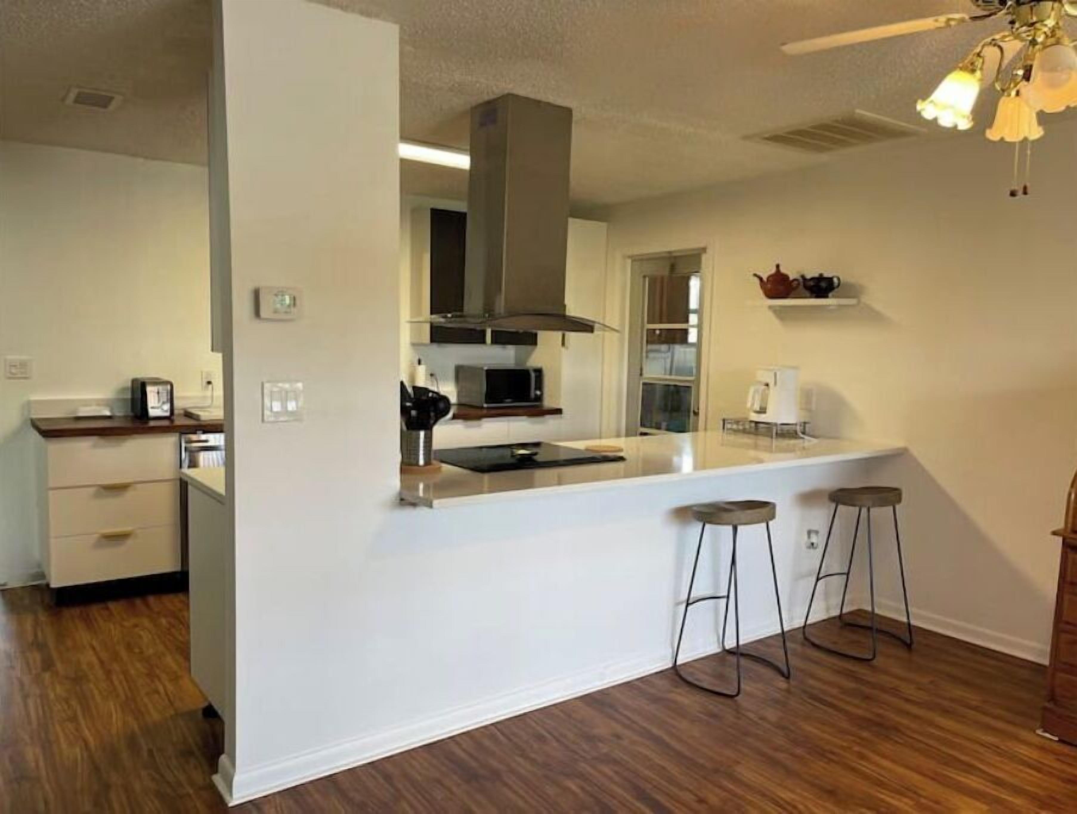 A modern kitchen with a central island, bar stools, and a microwave.
