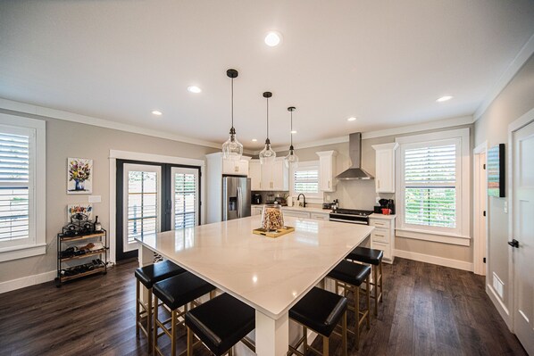 A spacious kitchen with a large island, pendant lighting, and a shoe rack by the window.