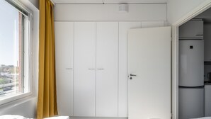 Une chambre d’hôtel comprenant un lit, une armoire, un coin cuisine et une fenêtre avec des rideaux.