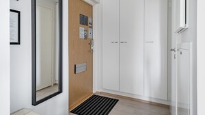 Un couloir avec un grand miroir, une porte en bois, une armoire blanche et un tapis noir sur le sol.