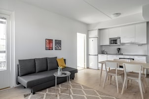 Un apartamento moderno con un sofá gris, una mesita redonda y una mesa de comedor de madera con sillas.