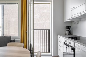Una cocina moderna con cafetera, un comedor con cama y vista a un edificio de ladrillo a través de una ventana.