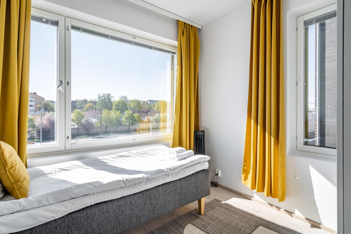 A bedroom with a bed, large windows, and yellow curtains.