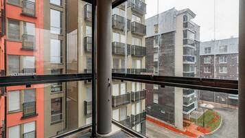 A multi-story residential building with balconies, a glass facade, and a visible courtyard with a bench and small trees.