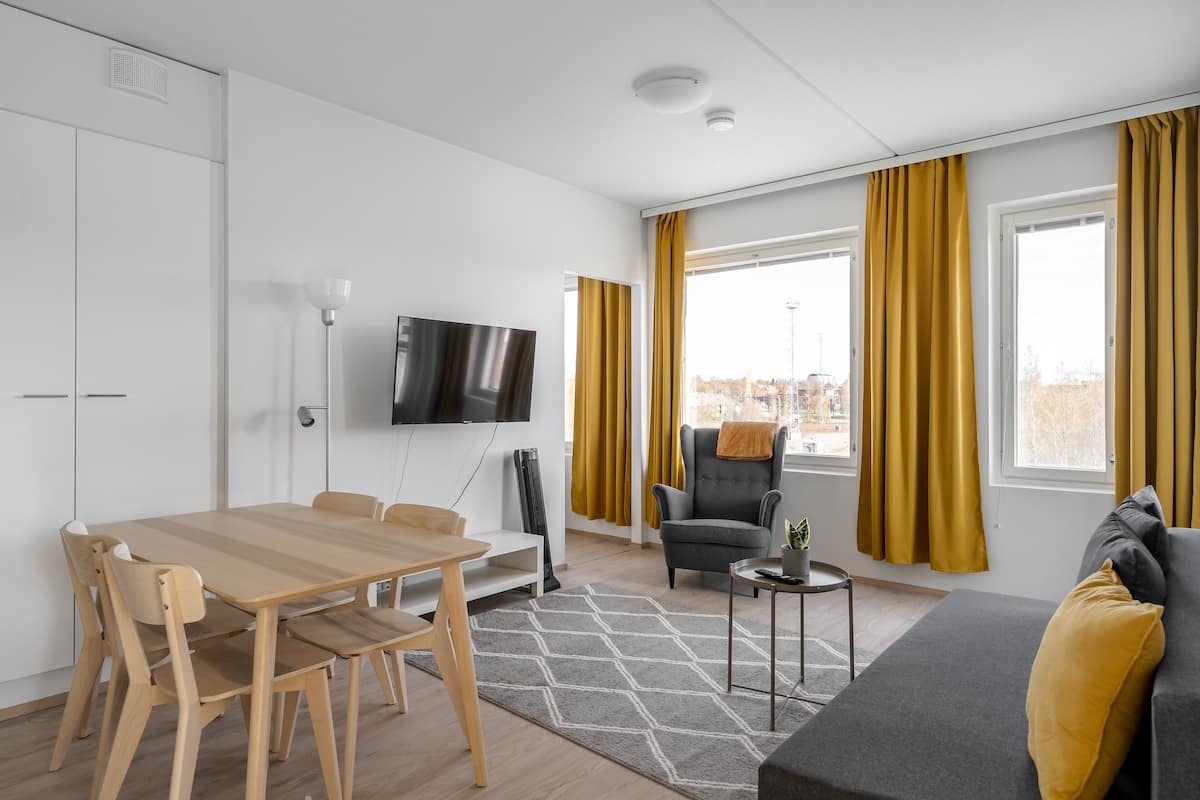 A modern living room with a sofa, a TV, a dining table with chairs, and a window with curtains.