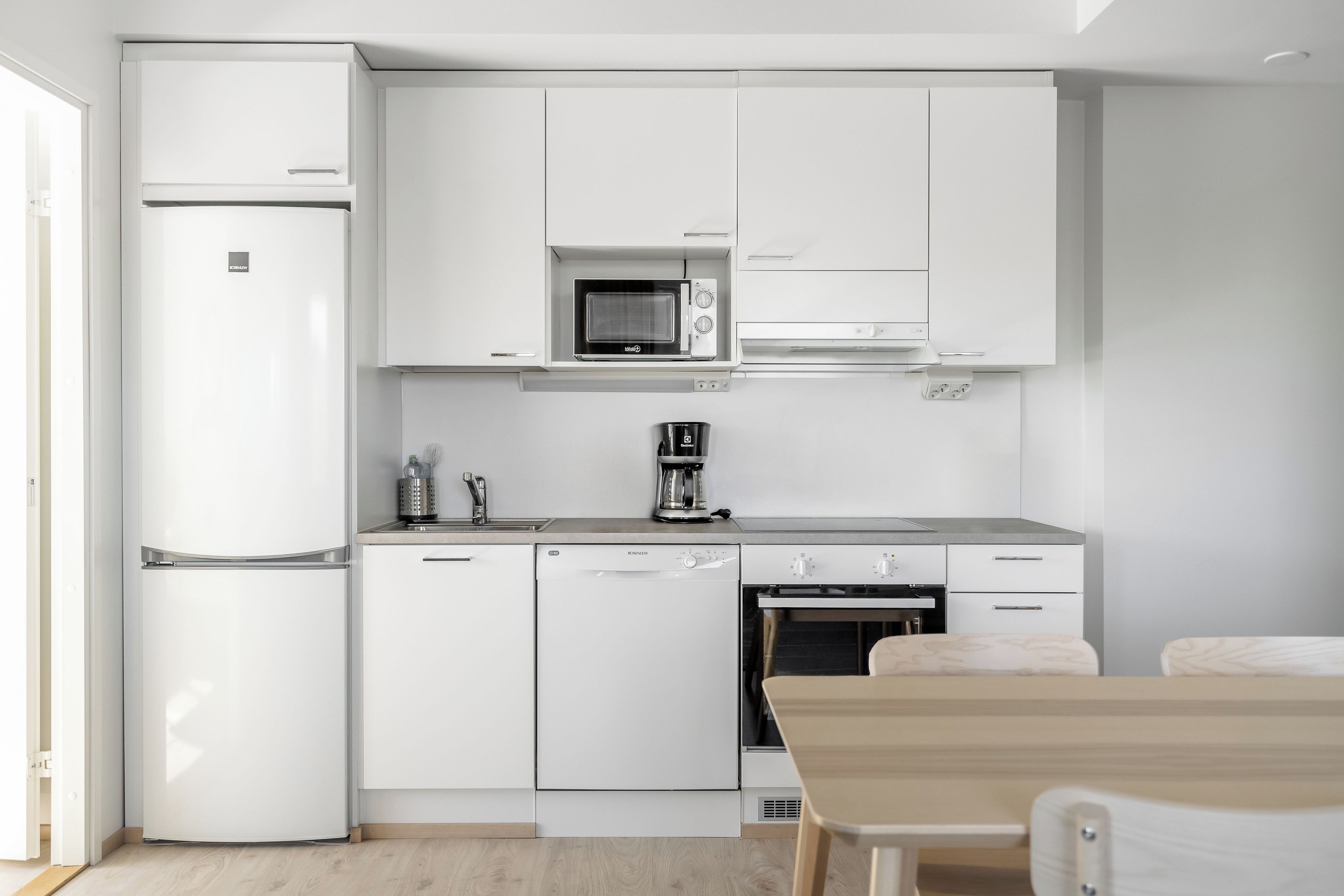 A modern kitchen with white cabinetry, a built-in microwave, a coffee machine, and a dishwasher.