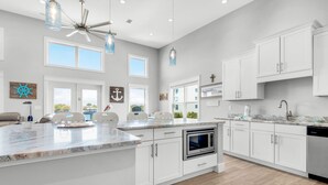 Una cucina moderna con mobili bianchi, una grande isola centrale e una ventola a soffitto.