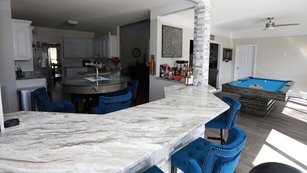 A modern kitchen with a marble island, blue bar stools, and a pool table in the living area. - Golf Course Retreat w/Sunroom, Pool Table & Patio (WARNER ROBINS)