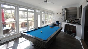 A pool table with a blue felt surface, a ceiling fan, and a view of the outdoors through large windows. - Golf Course Retreat w/Sunroom, Pool Table & Patio (WARNER ROBINS)