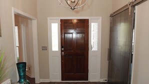 A hallway with a wooden door, a dark-colored sliding door, a chandelier, and a patterned rug. - Golf Course Retreat w/Sunroom, Pool Table & Patio (WARNER ROBINS)