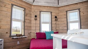 A bedroom with wooden walls, a bed with a red bedspread, two windows with blinds, and a shelf with a decorative item. - Legacy Lighthouse, Amish Country Ohio, Sugarcreek (Sugarcreek)