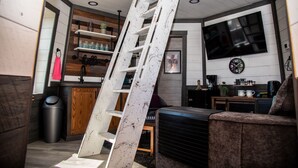 A living room with a white ladder, wooden cabinets, a TV, and a clock on the wall. - Legacy Lighthouse, Amish Country Ohio, Sugarcreek (Sugarcreek)