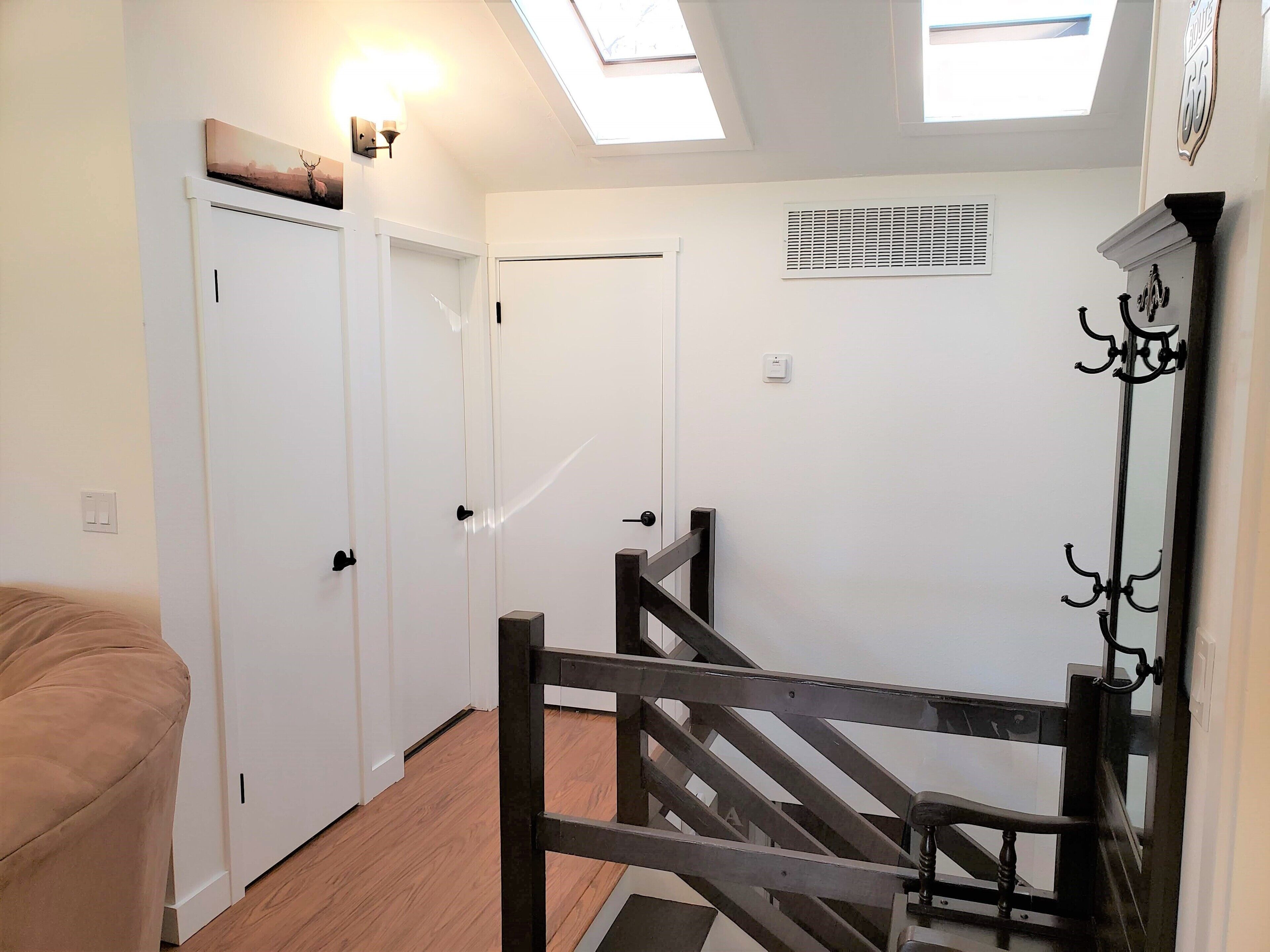 A hallway with a wooden staircase, white doors, and a skylight.