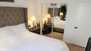 A neatly made bed with white linens, a tufted headboard, bedside lamps, a mirror, and a wardrobe. - Flagstaff Golf Course Condo - 9th Green of Continental Country Club (Flagstaff)
