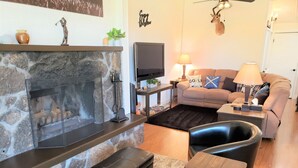 A cozy living room with a stone fireplace, a flat-screen TV, a comfortable sofa, and a coffee table. - Flagstaff Golf Course Condo - 9th Green of Continental Country Club (Flagstaff)
