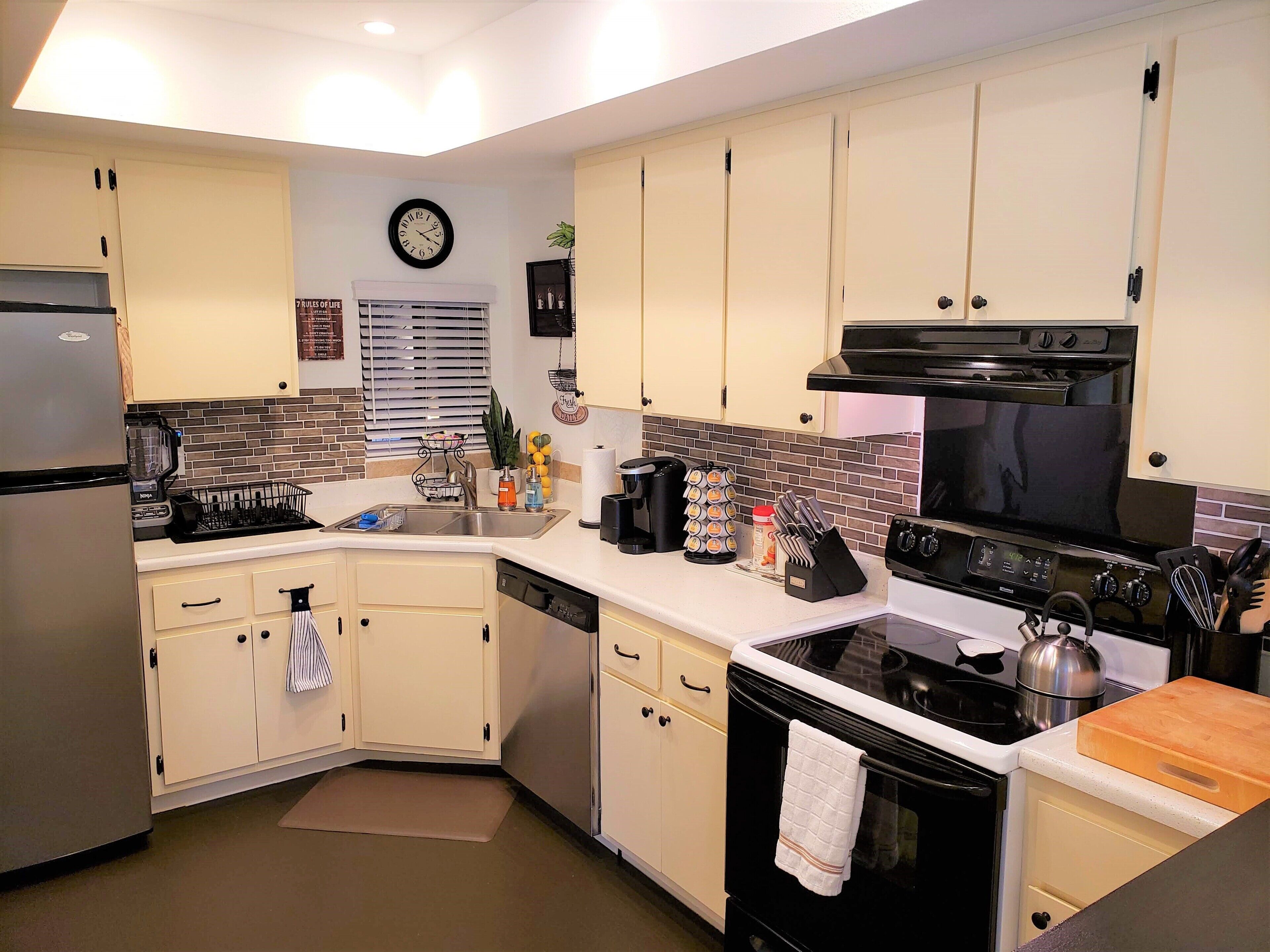 A modern kitchen with white cabinets, a stainless steel refrigerator, a black stove, and a microwave.