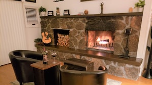 A cozy living room with a stone fireplace, two leather armchairs, a small table with a bottle and glass, and a guitar on the mantel. - Flagstaff Golf Course Condo - 9th Green of Continental Country Club (Flagstaff)