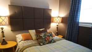 Un lit bien fait, recouvert d’une couverture à carreaux, avec deux lampes de chevet et une tête de lit.
