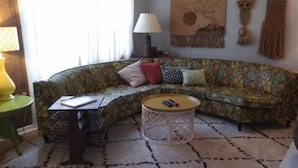 Un salon avec un canapé incurvé, une table basse ronde, un fauteuil vert, une lampe et un ventilateur de plafond.