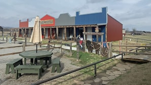 Een rustiek gebouw met een rood- en blauwe gevel, een bord met de tekst 'LAZY BUFFALO' en een houten omheining met picknicktafels ervoor.