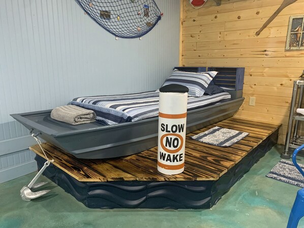 A bed with a 'SLOW NO WAKE' sign, a small boat-like structure, and a hammock. - Catch Zzz in Real Boat, Going Fishing Cabin near Wildlife Refuge Cache sleeps 3 (Cache)