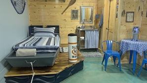 Een kleine kamer met een bed, een tafeltje met een stoel, een wastafel en een spiegel.