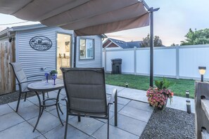 A patio area with a covered table and chairs, a small potted plant, and a sign on the wall. - Adorable cottage with king Size bed and a short distance to WW University (Walla Walla)